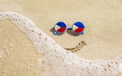 Sunglasses with flag of Philippines on a sandy beach. Nearby is a sea lightning and a painted smile. The concept of a successful vacation in the resorts of the Philippines.