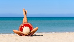 A slender tanned girl on the beach in a straw hat in the colors of the flag of Turkey. The concept of a perfect vacation in a resort in the Turkey. Focus on the hat.