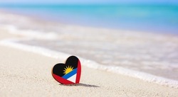 Flag of Antigua and Barbuda in the shape of a heart on a sandy beach. The concept of the best vacation in Antigua and Barbuda