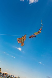 Colorful kites fly in the blue sky. They are tied with a rope to each other and fly in a single chain. Image with selective focus.