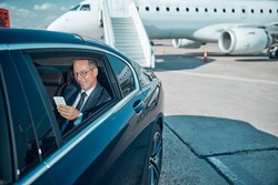 Smiling elegant man in glasses is using cell phone during transfer after trip by plane