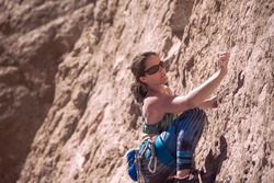 Female climber. Young adult fit woman climbing with rope a stone rock wall at sunny day. Concept of adventure and extreme sport outdoors. Climbing equipment and sportswear. Copyspace