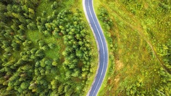 Aerial view of twisting road among the forest and trees. Sunset field in Lithuania.