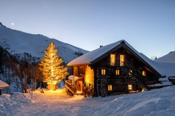 Dusk on a Holiday Hut in the Swiss Alps with Snow and Lighten up Tree