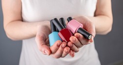 Woman is holding a variety of colorful bottles of nail polish in her hands. Closeup. Concept of choosing a color for manicure.