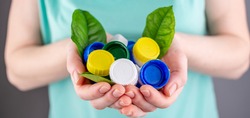 Hands are holding a handful of colorful plastic lids with green leaves. Concept of environmental pollution, eco friendly behavior, waste sorting and plastic recycling.
