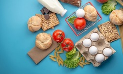Set of fresh products and a miniature shopping basket on a blue background top view. Online shopping concept, food delivery.