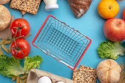 Set of fresh products and a miniature shopping basket on a blue background top view. Online shopping concept, food delivery.