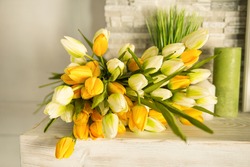 
A bouquet of beautiful yellow and white tulips, spring flowers, artificial flowers, like real ones, lie on a light wooden shelf at home
