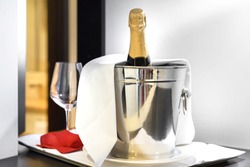 Bottle of cold wine or champagne in ice bucket on white table at hotel room. Wedding reception, holiday concept. Copy space.