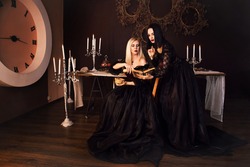Two witches perform a magic ritual love spell. Magic. The sorceress is a sorceress who reads the future in a magic book. fantasy beautiful girls in the image of a witch in a dark gothic room.
