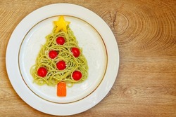 Christmas tree pesto spaghetti made it from spaghetti,pesto sauce,cherry tomato,parmesan cheeses,yellow bell pepper and carrot on plate with wooden background.Art food idea for Christmas dinner