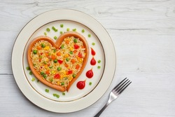 Fried rice with carrots,onions,tomatoes,green peas,spring onions,eggs and soy sauce in heart shaped sausage on plate with wooden background.Healthy food idea for Valentine's day.Top view.Copy space

