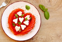 Valentine Italian Caprese salad with heart shaped tomatoes,heart shaped mozzarella cheeses,basil leaves and origano on plate with wooden background.Love Italian food concept for Valentine's day