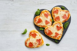 Heart shaped mini pizzas with heart shaped pepperoni on heart shaped slate plate with white wood background.Creative art food idea for celebrate Valentine or Mother day.Top view.Copy space