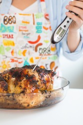 Young woman measuring whole roasted chicken temperature with digital meat thermometer 