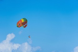 Bright parachute against the sky. Parasailing is an extreme sport, people fly by parachute against the blue sky. Marine entertainment, bright parachute, blurry figures of people. Copy space.