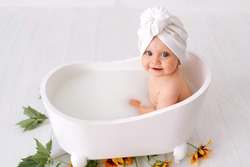 One year old baby girl takes bath. In blue swimming cap. Bathroom. The girl bathes in a basin. Clothes are dried on a hanger. Bath screens.