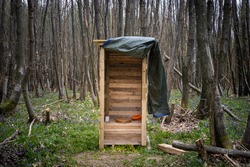 Wooden outhouse compost toilet with toilet seat, toilet paper and door curtain outdoors in the woods.