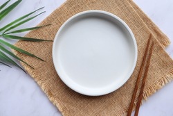 Empty white plate with wooden chopsticks on the sackcloth 