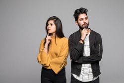 Portrait of serious thinking young loving indian couple isolated over white wall background looking aside.