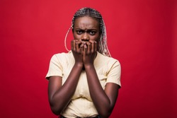 Headshot of beautiful scared young dark-skinned European woman closing mouth not to scream, feeling frightened and terrified, her eyes and look full of fear and terror isolated on red background