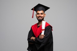 education, graduation and people concept - happy indian male graduate student in mortar board and bachelor gown with diploma over grey background