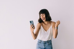 Portrait of a happy joyful girl holding mobile phone and celebrating a win isolated over white background