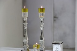 A pair of Shabbat candles are lit with oil on silver candlesticks and one low candle, and a charity cup of silver on the side. A Jewish custom on Shabbat night before sunset.