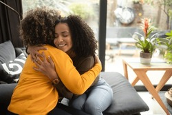An African-American female psychotherapist comforts the teenage female patient by hugging her. She is smiling because they have made progress. Both of them have the afro hairstyle.