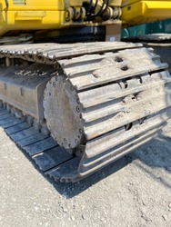 Dirty and rusty excavator track pad and grouser pad with top carrier rollers and track chain with sprocket at construction site
