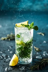 Fresh Mojito cocktail with lime, rosemary, mint and ice in jar glass on dark blue background. Studio shot of drink in freeze motion, drops in liquid splash. Summer cold drink and cocktail