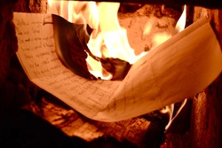 a sheet of paper is burning in the fireplace, a bright flame and firewood.  the letter burns in the fire