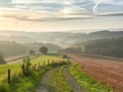 Rural landscape in the German city of Velbert at sunrise in the Bergisches Land region. A dirt road in the foreground and hazy woods in the background