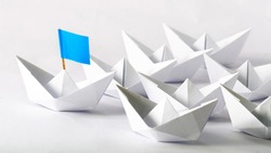 Leadership concept. Blue flag Origami White Paper boat (ship) leading the others.  One leader ship leads other ships.
