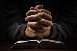 Praying man hands and bible on desk.