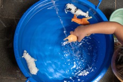 a toddler is playing with animal toys while taking a bath with a blue bucket of water