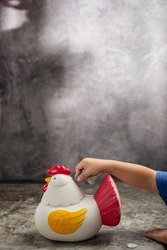 a toddler is putting a coin into a piggy bank in the shape of a chicken