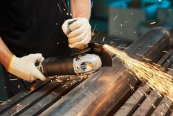 angle grinder for cutting metal, stones and ceramics. male hands in gloves cut a piece of iron pipe with sparks with a typewriter