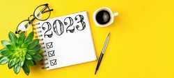 New year resolutions 2023 on desk. 2023 resolutions list with notebook, coffee cup on yellow table. Goals, resolutions, plan, action, checklist concept. New Year 2023 template, copy space