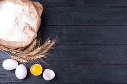 Baking background. Flour in paper bag, wheat and eggs on dark wooden table. Ingredients for cooking homemade baking. Top view. Copy space