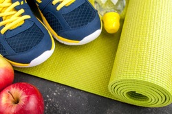 Yoga mat, sport shoes, apples, bottle of water on dark background. Concept healthy lifestyle, healthy eating, sport and diet. Sport equipment. Copy space