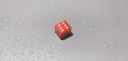 isolated single red plastic ludo gaming cube rolling dice with six white number dots on wet grey background table surface. winner, success and luck concept. closeup top view.