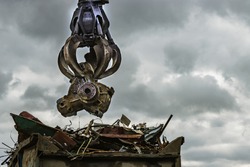 An excavator loads scrap metal into the back of a truck at a landfill or recycling center.