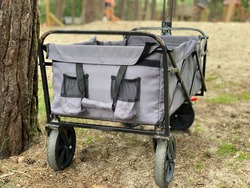 Folding transport cart for camping equipment -  grey trolley stand near tree on the grass land on day. Camping outside  