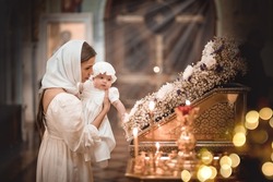 a mother with a small child in a temple or church prays near an icon and candles or came to a service in the Russian Orthodox church, the baptism of a baby in a baptismal white outfit