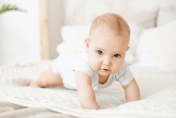 close-up of a happy baby on a white cotton bed in a bright bedroom, a small smiling baby boy or girl crawling