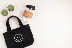 Black organic cotton cloth eco bag and reusable glass coffee cup on white background. Zero waste sustainable lifestyle. Plastic free concept. Flatlay, top view