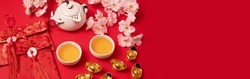 Chinese new year festival decoration over red background. Traditional lunar new year flat lay with green tea, red envelopes, gold ingots with text meaning fortune, prosperity, wealth. Top view