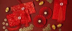 Chinese new year festival decoration over red background. Traditional lunar new year red pockets, paper fans, coins, gold ingots with text meaning fortune, prosperity, wealth. Flat lay, top view